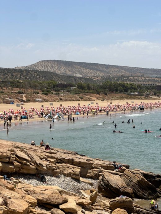 Beach with red and white umbrellas and surfers in the bay