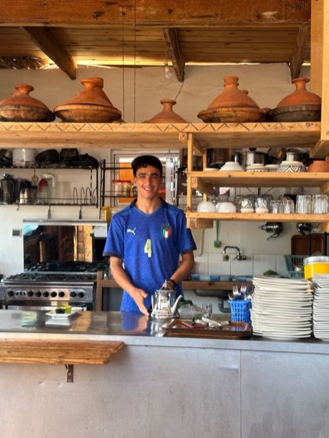 Smiling cook in the villa kitchen with tajines on the shelf